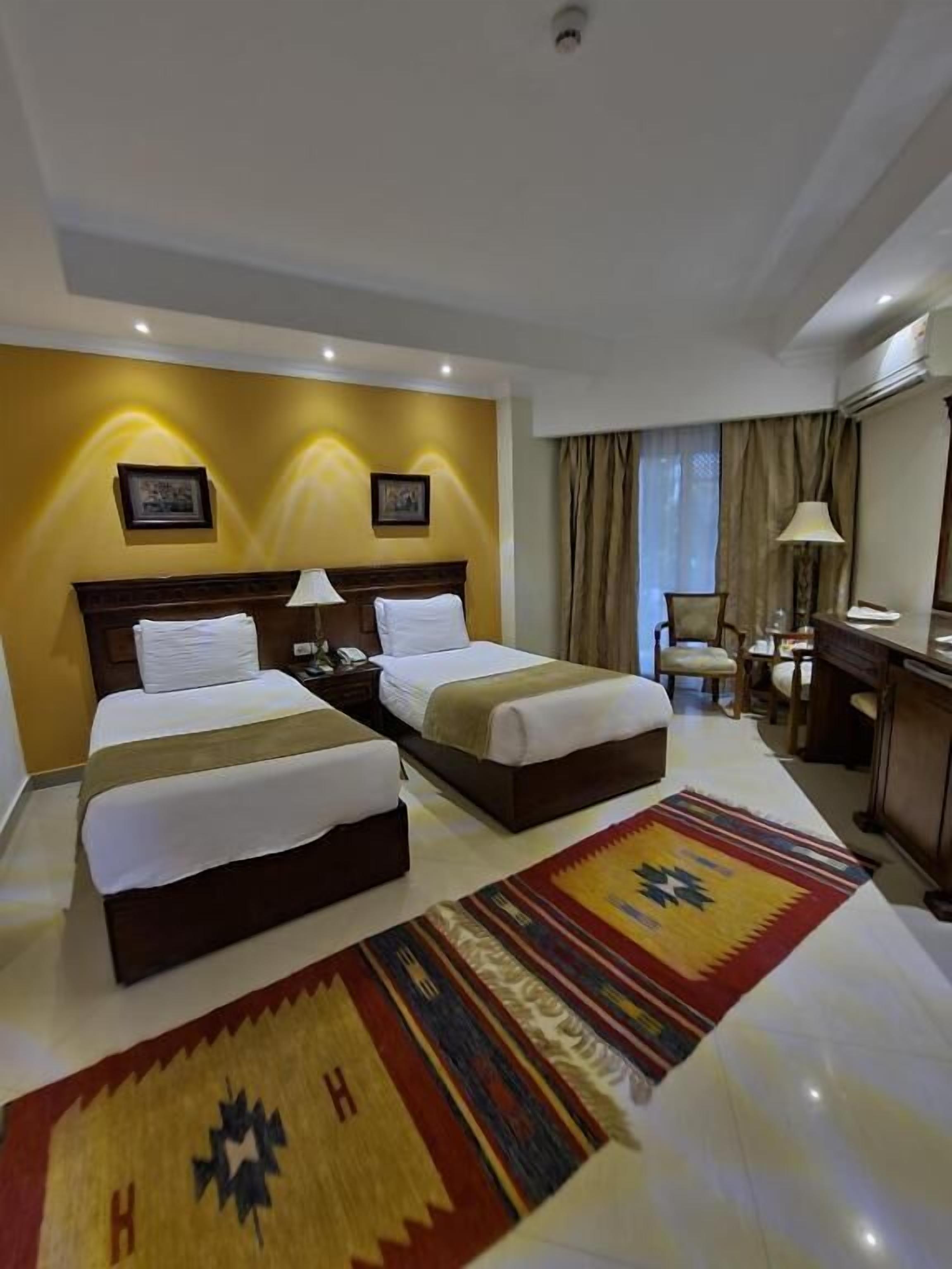 A hotel room with two beds, a desk, a chair, and a large rug.