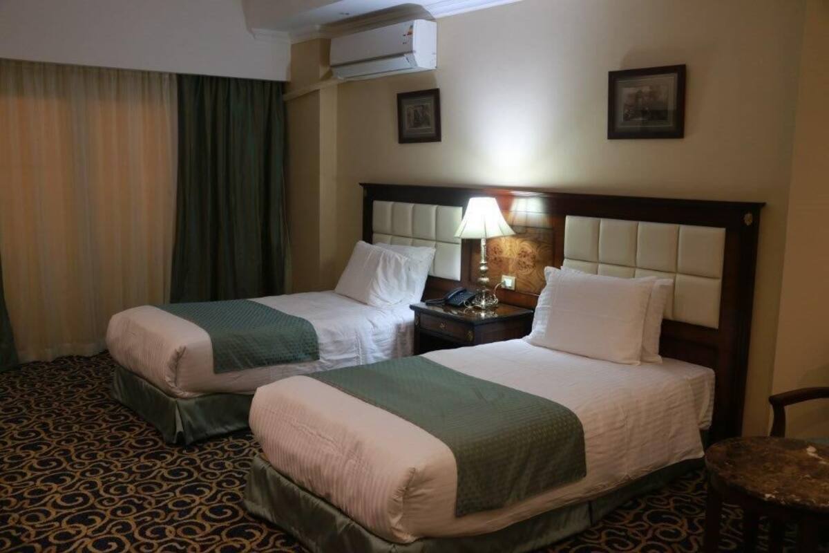 A hotel room with two beds, a nightstand with a lamp, and a patterned carpet.