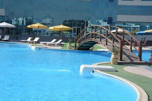 A swimming pool with lounge chairs and umbrellas, surrounded by a modern building with glass windows. - The Guard Hotel (Cairo)