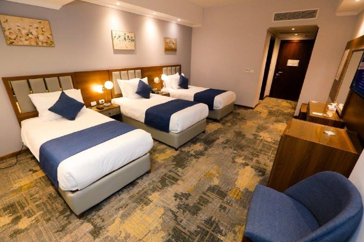 A hotel room with three beds, a desk, and a chair.