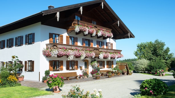 Un caratteristico chalet con un balcone decorato da fiori, un vialetto lastricato e un giardino con piante in vaso.