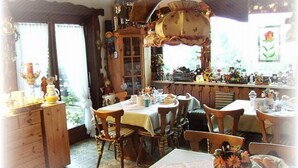 Un coin repas chaleureux, avec des meubles en bois, une grande fenêtre agrémentée de rideaux et divers objets décoratifs disposés sur des étagères.