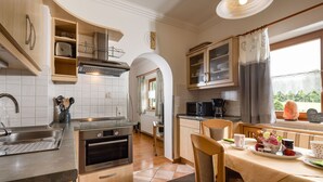 A kitchen with a built-in oven, microwave, and sink. There is a dining table with chairs and a window with curtains. - Vacation apartment Wiesentraum, for 1-2 persons (Berchtesgaden)