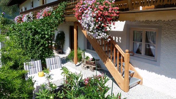 A traditional chalet with a wooden staircase, outdoor seating, and hanging flower baskets. - Ferienwohnung II 65 qm°, mit zwei extra Schlafzimmer mit Süd-Balkon (Aschau im Chiemgau)
