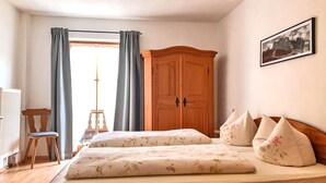 A bedroom with a wooden bed, a wooden wardrobe, a chair, and a window with curtains. - Ferienwohnung II 65 qm°, mit zwei extra Schlafzimmer mit Süd-Balkon (Aschau im Chiemgau)