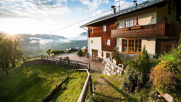 Eine zweistöckige Chalet mit einem Balkon, umgeben von üppiger Vegetation und einer Bergkulisse.