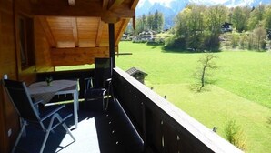 Un balcon en bois avec une table et des chaises, donnant sur un champ verdoyant et des montagnes.