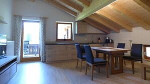 Un vaste espace de vie doté d’un plafond en bois, d’une table à manger avec des chaises, d’un coin cuisine avec des placards et d’une grande fenêtre qui laisse entrer la lumière naturelle.