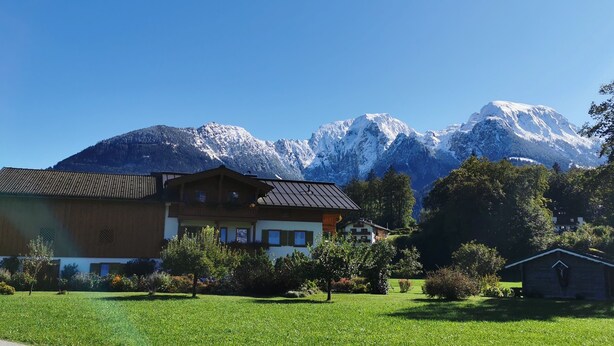 Un bâtiment de style chalet, doté d’un toit en pente, entouré d’une pelouse bien entretenue et d’arbres, avec des montagnes enneigées en arrière-plan.