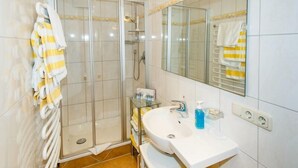 Une salle de bain avec une douche à parois de verre, un lavabo blanc avec un miroir au-dessus, et des serviettes suspendues sur un porte-serviettes.