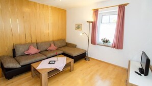Un salon comprenant un canapé, une table basse en bois, un meuble pour la télévision et une fenêtre avec des rideaux.