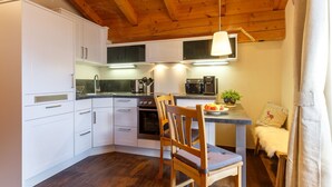 A modern kitchen with white cabinets, a wooden ceiling, and a dining area with a table and chairs. - Apartment Rauschberg 59 sqm, 1 sep. Bedroom, 1 living room, balcony, max. 2 pers (Ruhpolding)