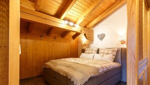 A cozy bedroom with a wooden ceiling, a bed with a checkered blanket, and two wall-mounted lamps. - Apartment Rauschberg 59 sqm, 1 sep. Bedroom, 1 living room, balcony, max. 2 pers (Ruhpolding)