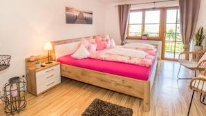 Una camera da letto con un letto di legno, un comodino, una lampada, una finestra con tende e vista sull'esterno.
