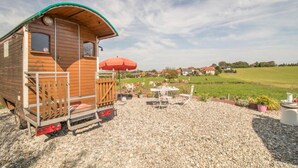 Una baita di legno con tetto verde, un ombrello rosso e un patio sterrato con mobili da esterno.