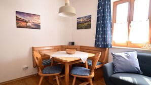 Een gezellig hoekje met een houten tafel en stoelen, een blauwe bank en een raam met gordijnen.