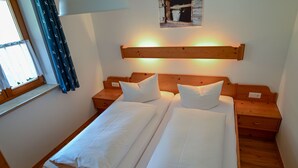 Een tweepersoonsbed met witte lakens, een houten hoofdbord, nachtkastjes en een raam met gordijnen.