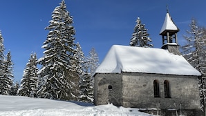 Une petite église en pierre, dotée d’un clocher, entourée d’arbres couverts de neige.
