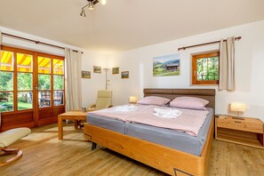 A bedroom with a wooden bed, a chair, a bedside table, and a window with curtains.
