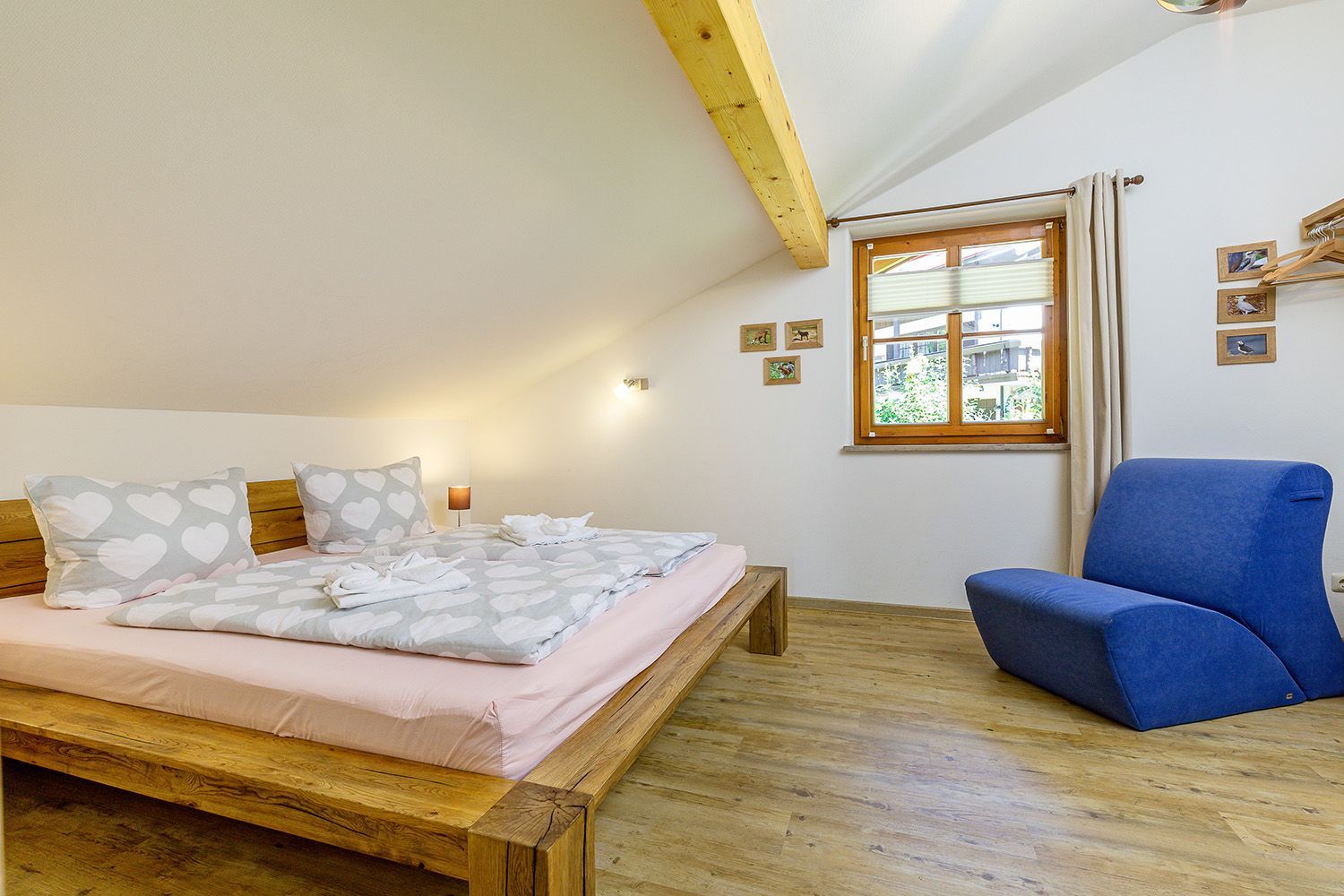 Un dormitorio con una cama de madera, una silla azul y una ventana con vistas a edificios.