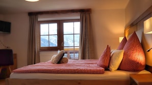 Ein Schlafzimmer mit einem hölzernen Bett, karierter Bettwäsche und einem Fenster mit Blick auf die Berge.