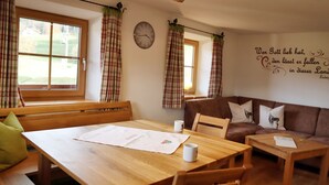 Ein gemütliches Zimmer mit Holztisch, Bank und Sofa. Eine Uhr und ein Wandspruch sind sichtbar.