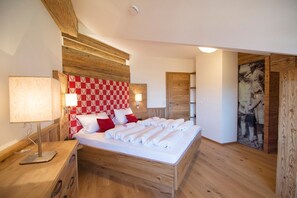 A bedroom with a wooden headboard, a bed with white linens, a bedside table with a lamp, and a wall-mounted shelf.