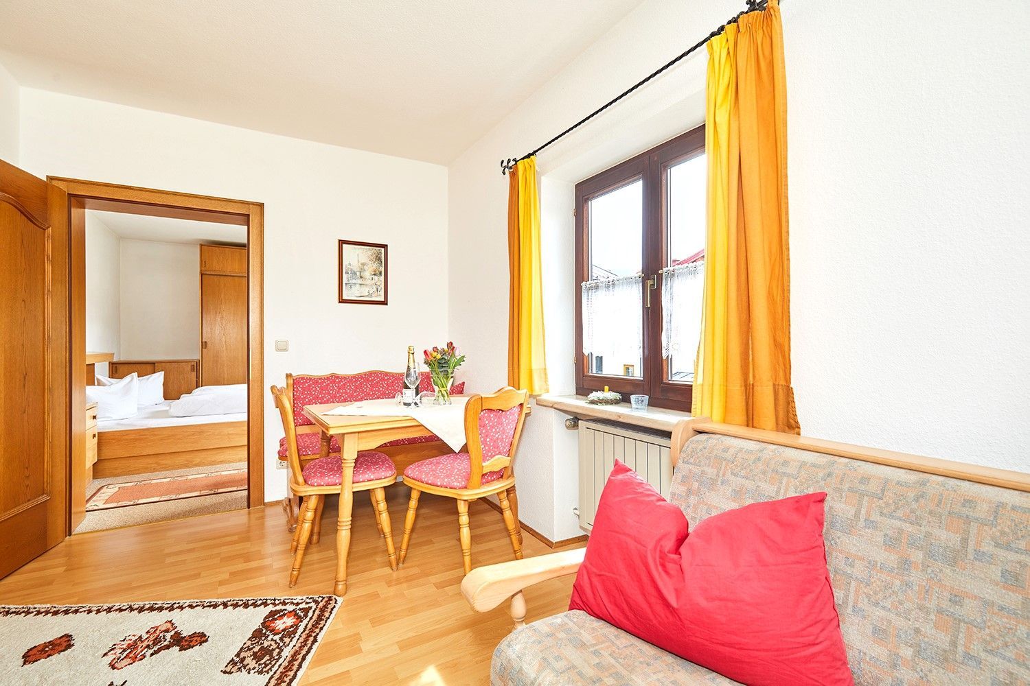 A room with a bed, a dining table with chairs, a sofa, and a window with curtains.