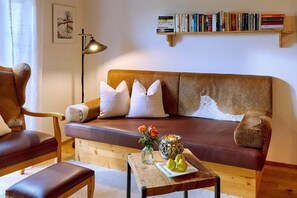 A cozy living room with a brown leather sofa, a wooden coffee table with a vase and pears, and a bookshelf filled with books. - Ferienwohnung "Mohnblume", 47 qm Obergeschoss, 1 separates Schlafzimmer (Höslwang)