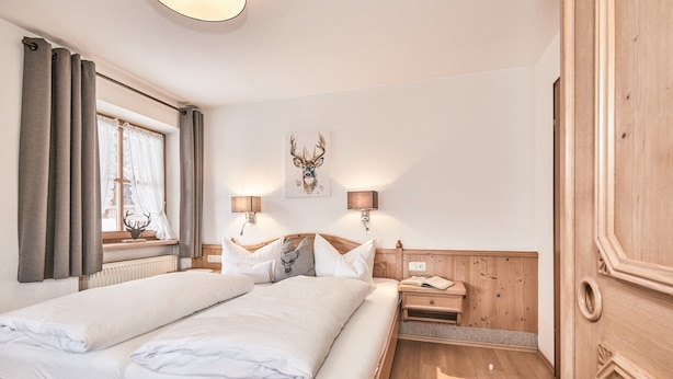 A double bed with white linens, a wooden headboard, two bedside lamps, a wall-mounted deer head artwork, and a wooden wardrobe.