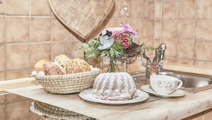 A kitchen counter with a wooden heart decoration, a basket of bread, a bundt cake, a floral arrangement, and a decorative cup.