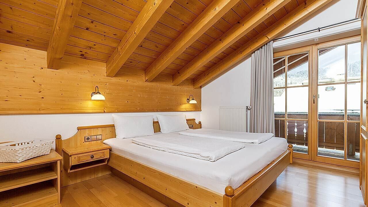 A wooden bedroom with a bed, nightstands, and a window with a view.