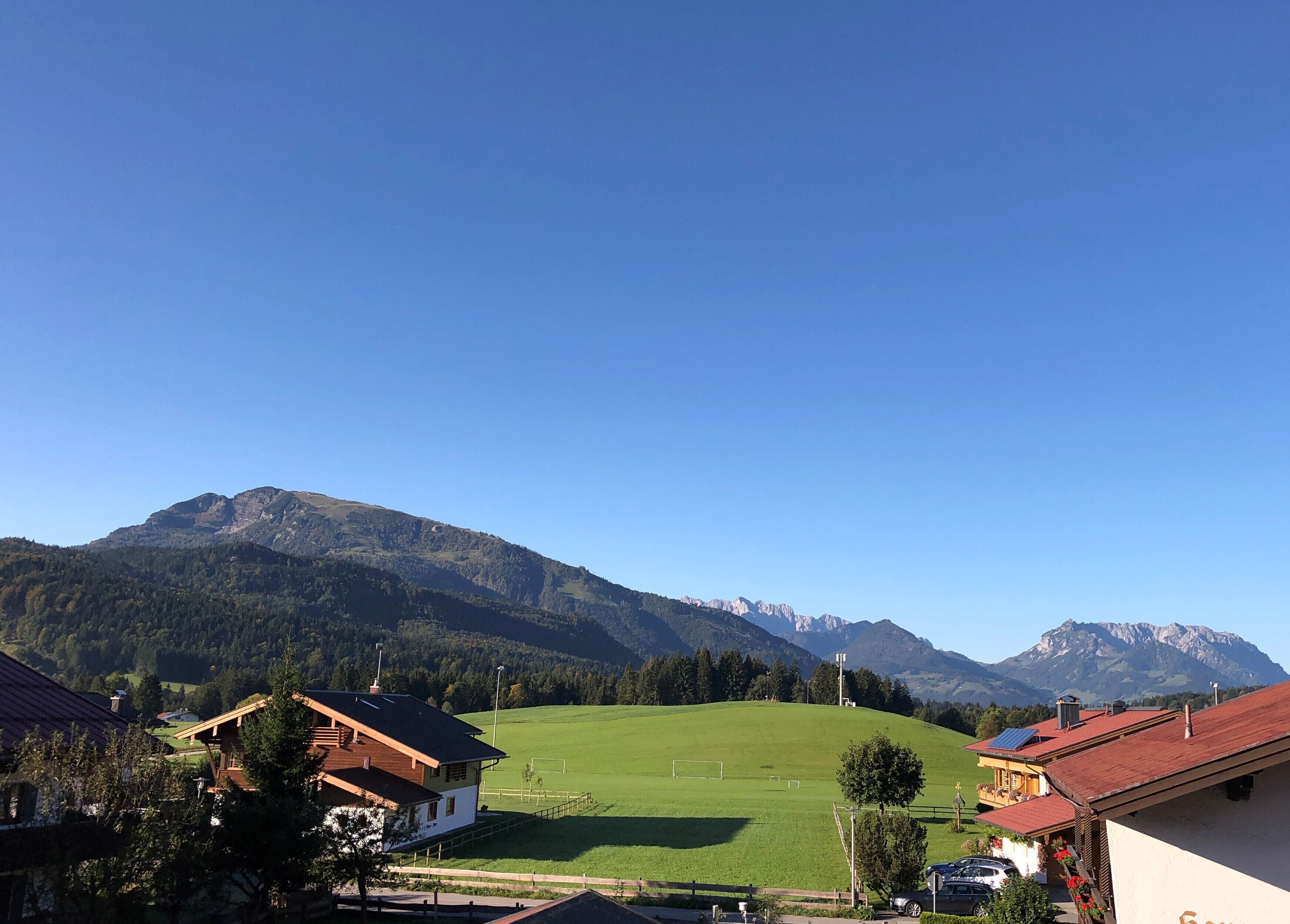 A rural landscape with a green field, houses with red roofs, and mountains in the background.