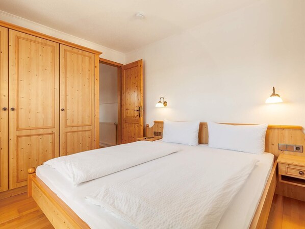 Une chambre à coucher avec une grande armoire en bois, un lit double avec une literie blanche et deux lampes de chevet.