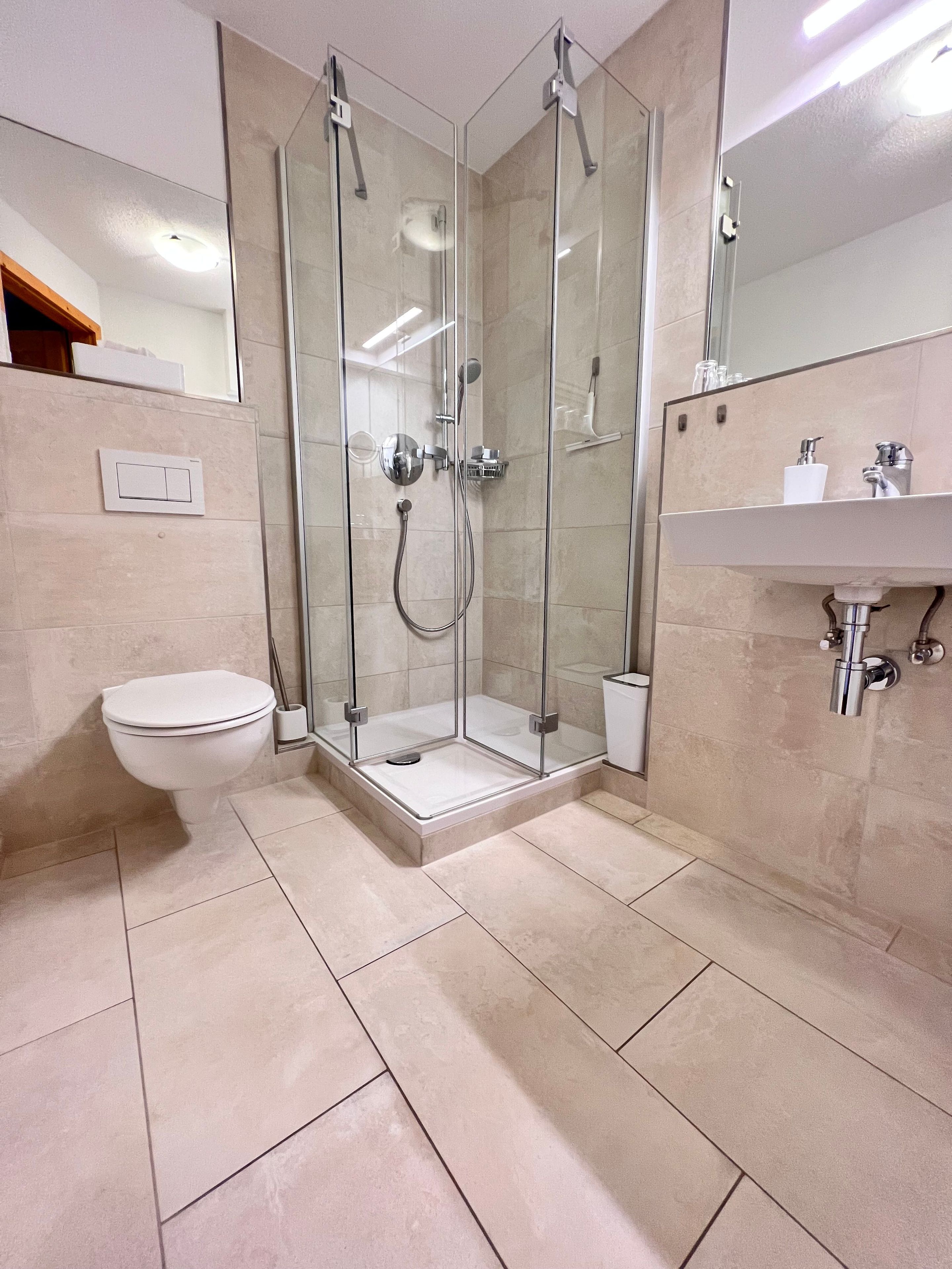 Un bagno moderno con doccia vetrata, un water e un lavabo con specchio soprastante.