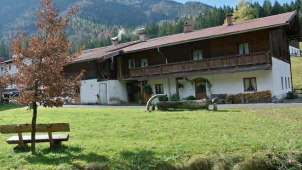 En traditionell alpchata med en träbalkong, en bänk av sten och en bergskuliss i bakgrunden.