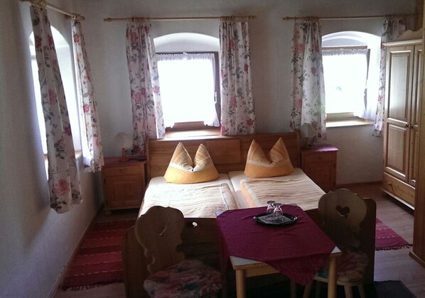 A bedroom with two beds, a wooden nightstand, a table with a red tablecloth, and floral curtains. - Vacation home for 10 people, 5 bedrooms, 200 m² (Inzell)