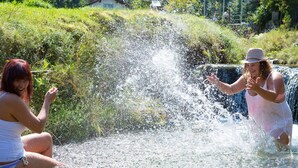 Två personer leker i ett grunt vattenområde med ett vattenfall i bakgrunden.