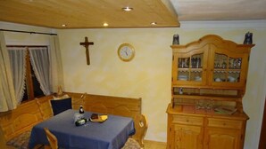 Un comedor con una mesa y sillas de madera, un armario de madera con puertas de cristal, un reloj de pared y una cruz de madera.
