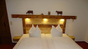 Cama doble con sábanas blancas, cabecero de madera con siluetas de vacas y mesitas de noche.