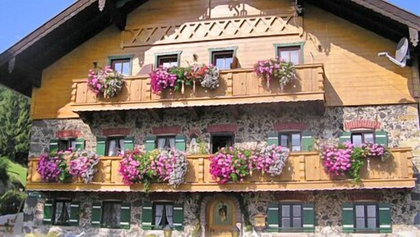 En traditionell chalet i trä med balkonger prydda med blommor, stenväggar och en trädörr.