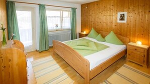 Quarto com painéis de madeira, uma cama, cortinas verdes, uma mesa de cabeceira e um radiador.