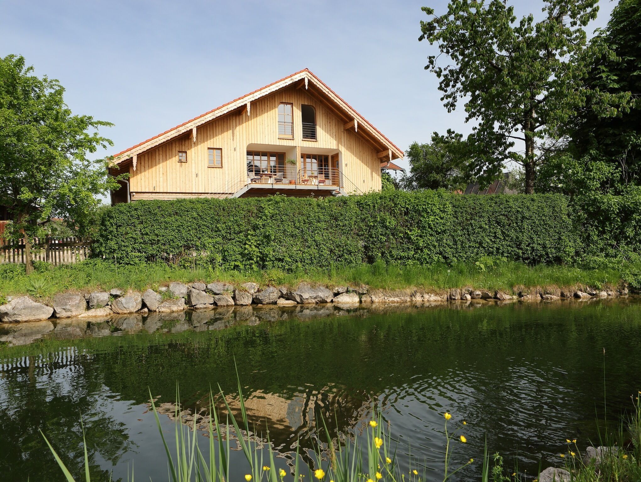 Ein Holzhaus mit Balkon, neben einem Teich mit Seerosen und gelben Blüten.
