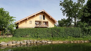 Ein Holzhaus mit Balkon, neben einem Teich mit Seerosen und gelben Blüten.