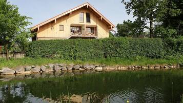 Ein Holzhaus mit Balkon, neben einem Teich mit Seerosen und gelben Blüten.