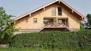 Eine Holzhütte mit geneigtem Dach, einem Balkon mit Sitzgelegenheit und einem großen Fenster.