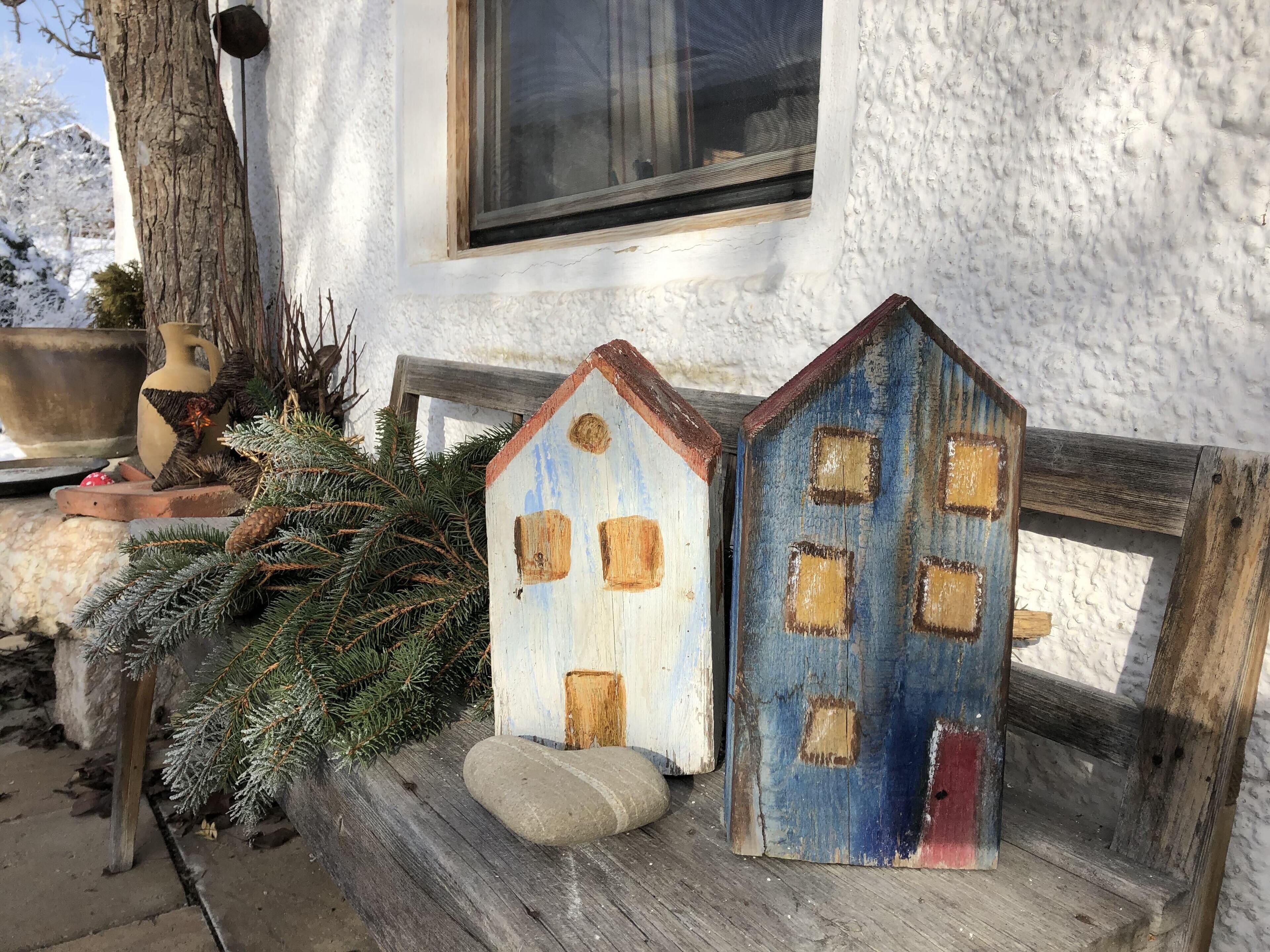 Two rustic wooden houses with windows and doors, placed on a wooden bench outside a white building with a window.