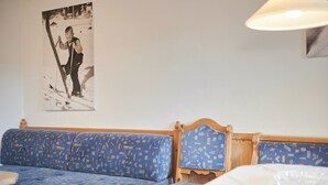Une pièce avec un canapé bleu à motifs, une tête de lit en bois et une table recouverte d’une nappe blanche.