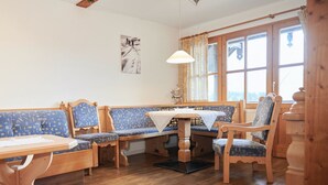 Une pièce chaleureuse, meublée de meubles en bois, avec une table recouverte d’une nappe blanche et une fenêtre agrémentée de rideaux.