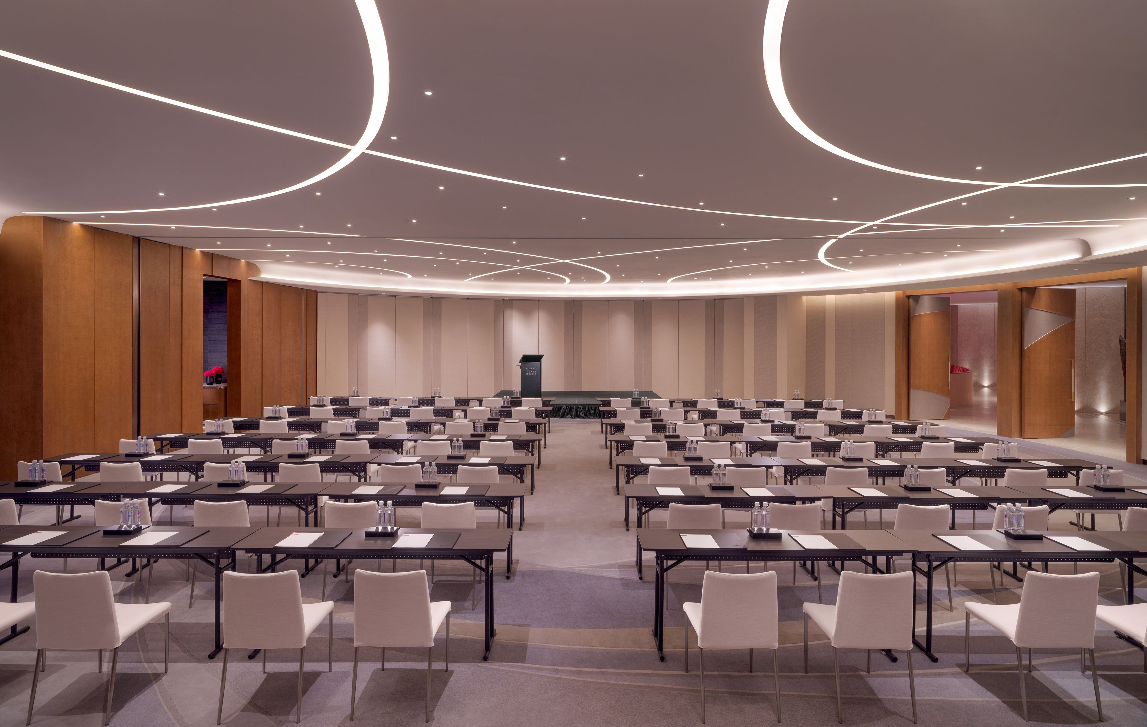 A conference room with multiple tables and chairs, a podium, and a modern ceiling design.